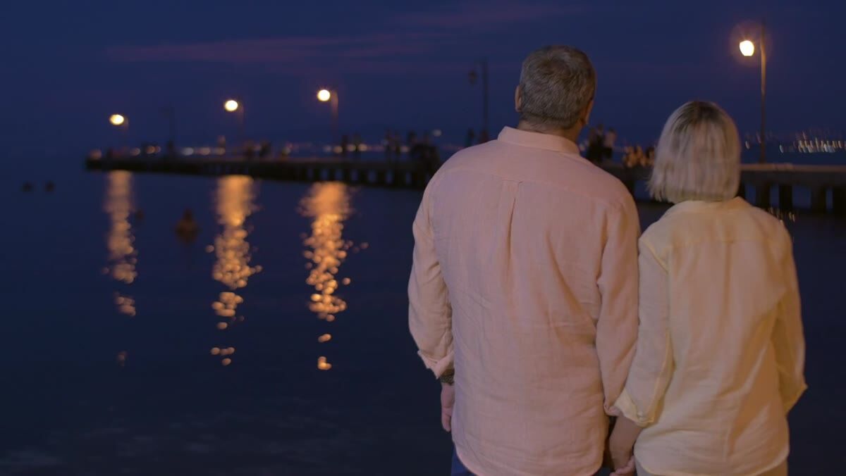 An older couple walking together by the water on a bright day